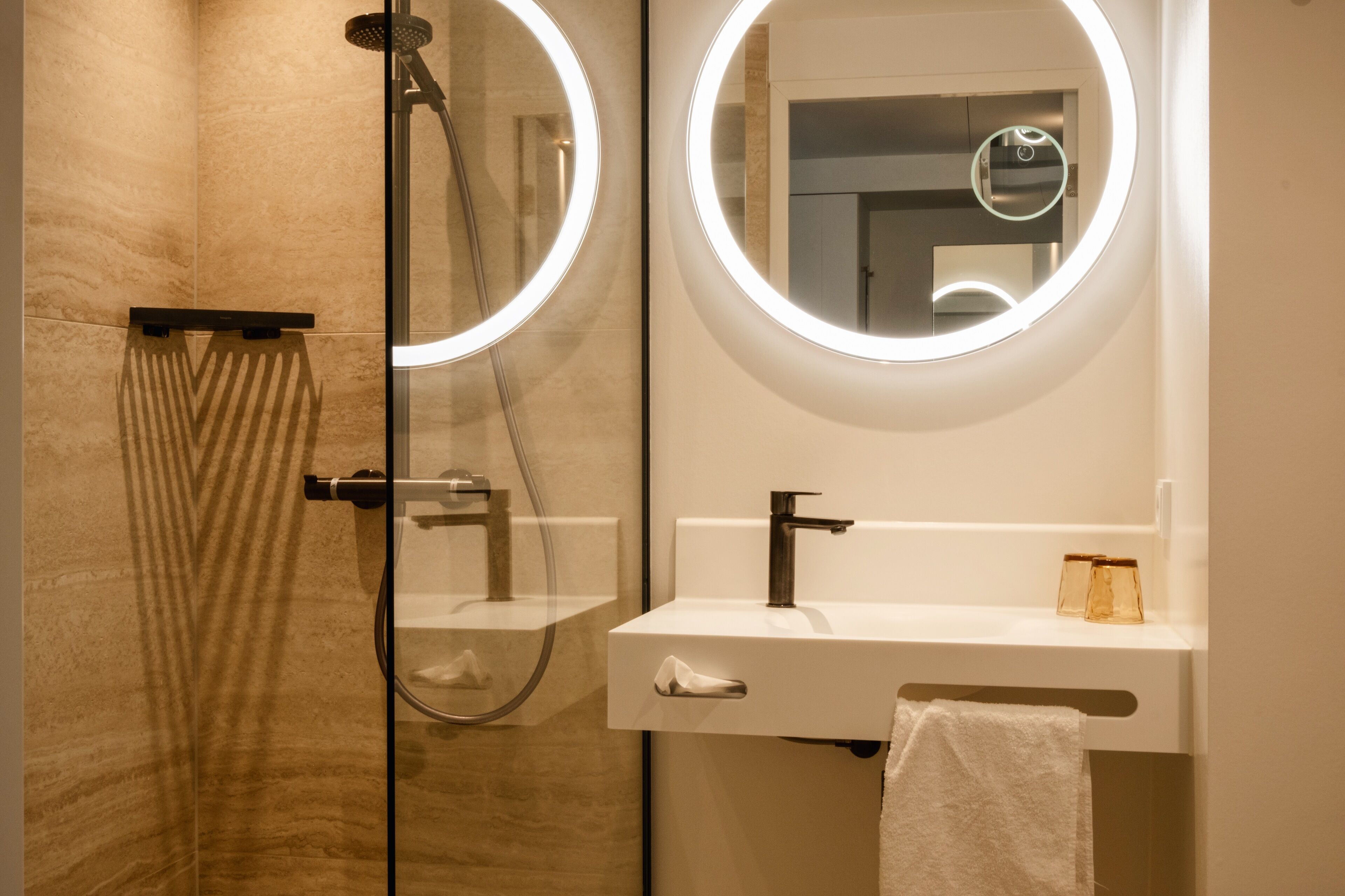 Une salle de bain moderne avec une douche à l’italienne, un lavabo blanc avec un miroir et une serviette accrochée au mur.