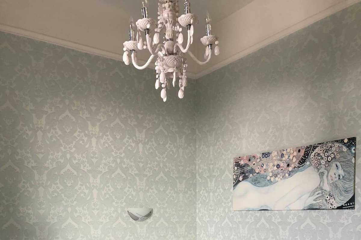 A bedroom with a bed, a nightstand, a wall clock, a chandelier, and a painting.