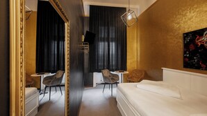 Quarto de hotel com cama, uma mesinha, duas cadeiras, televisão e um quadro na parede.