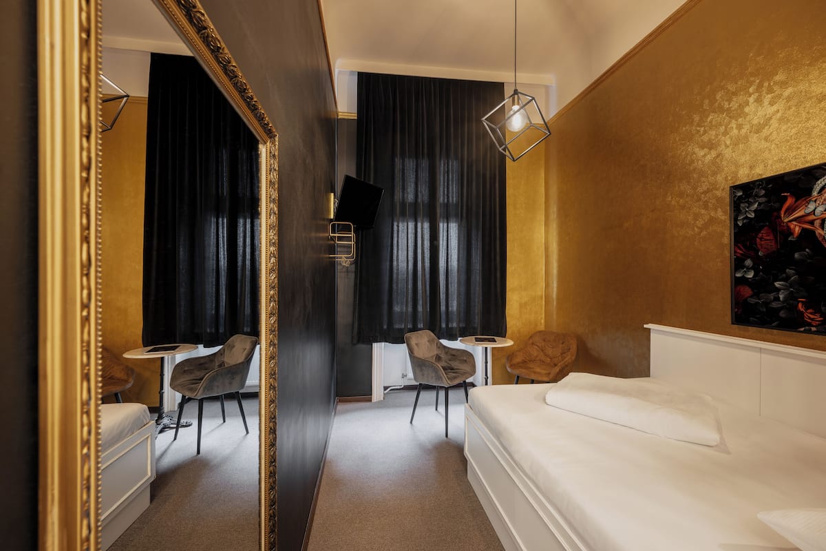 A hotel room with a bed, a small table, two chairs, a TV, and a painting on the wall.
