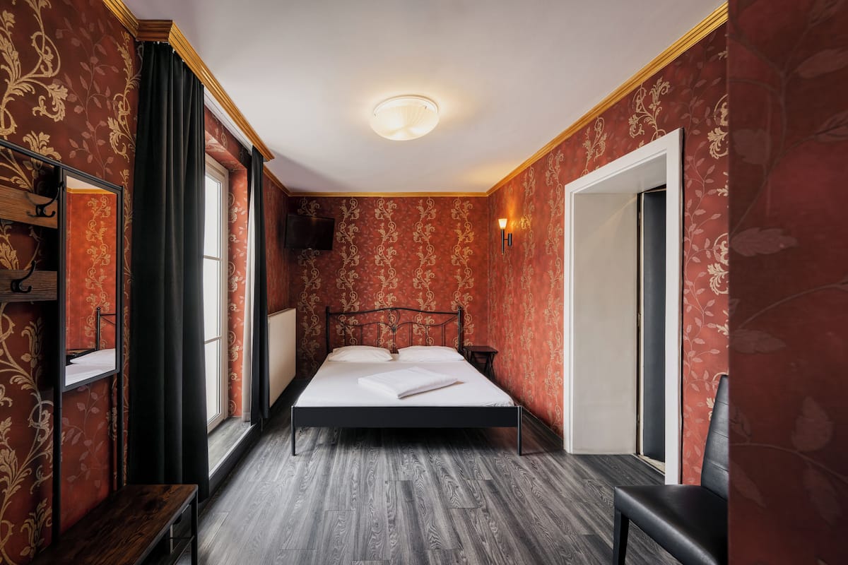 A room with a bed, a bedside table, a mirror, and a window with curtains.