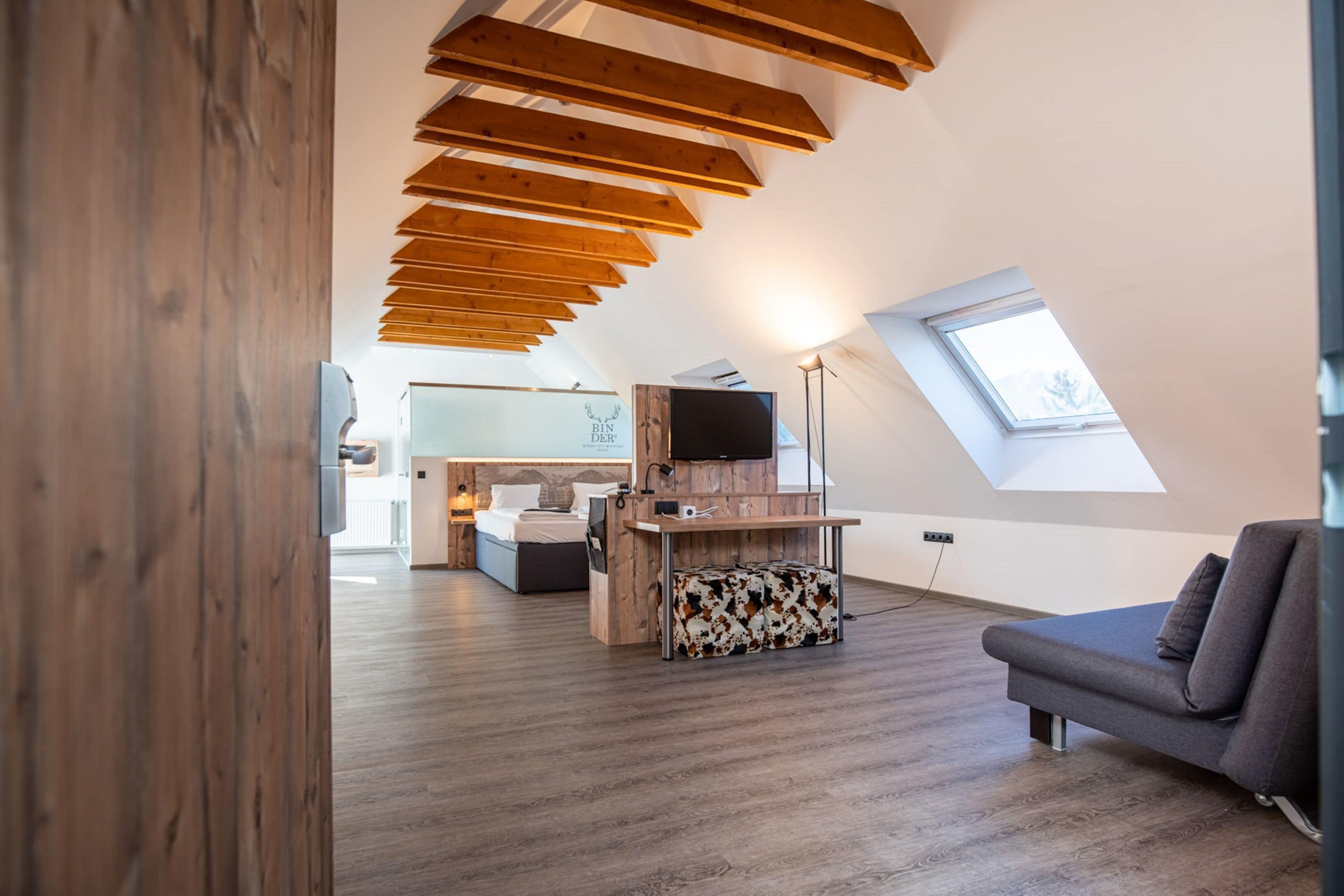 Un loft moderno con techo inclinado, vigas de madera, un área de estar acogedora, una kitchenette y un tragaluz grande.
