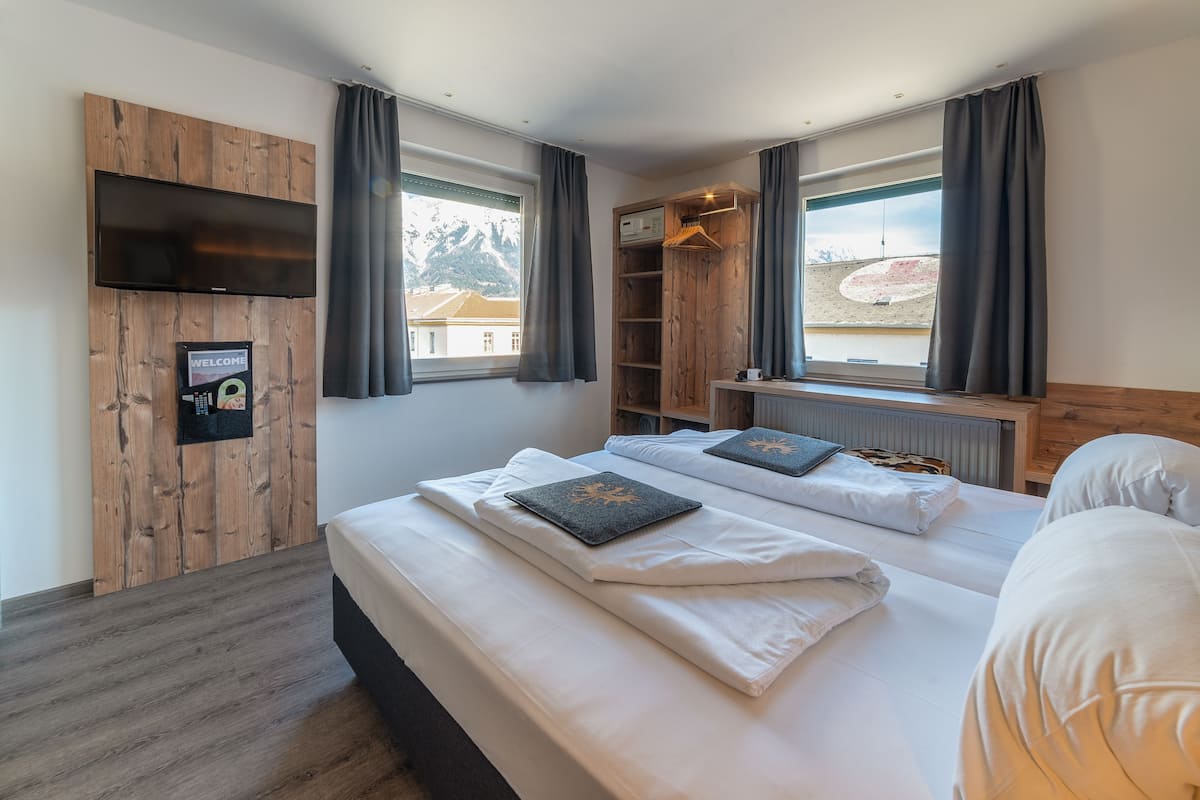 Una habitación de hotel moderna con una cama grande, un televisor montado en una pared de madera, un armario y vistas a la montaña a través de la ventana.