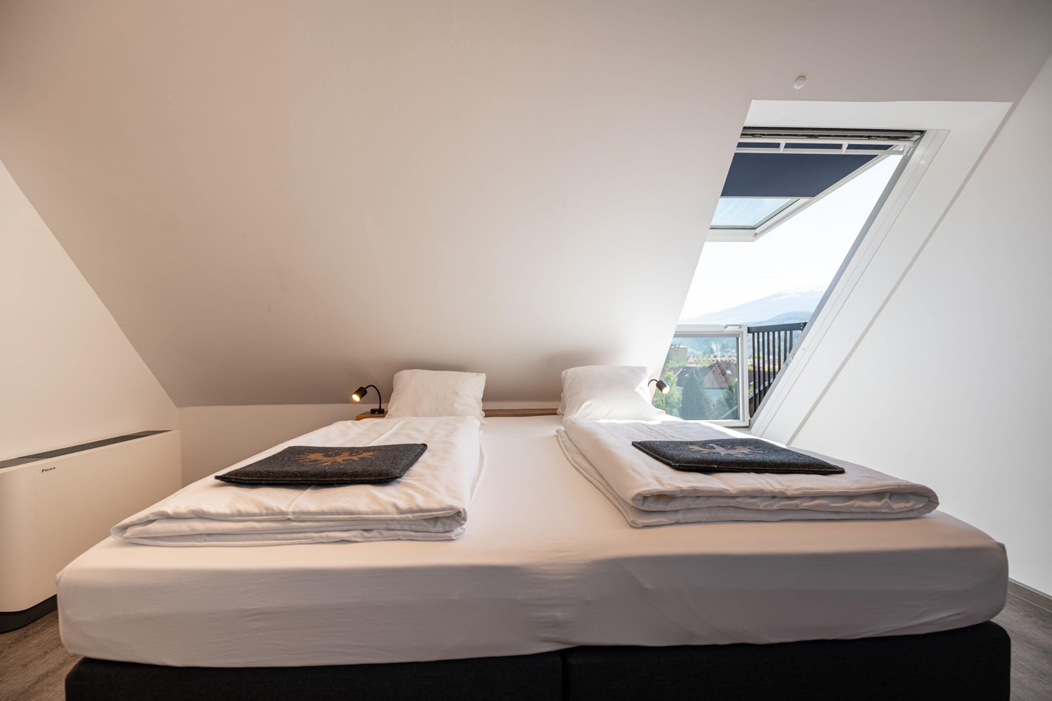 Une chambre moderne avec deux lits, une lucarne et une vue sur l’extérieur.