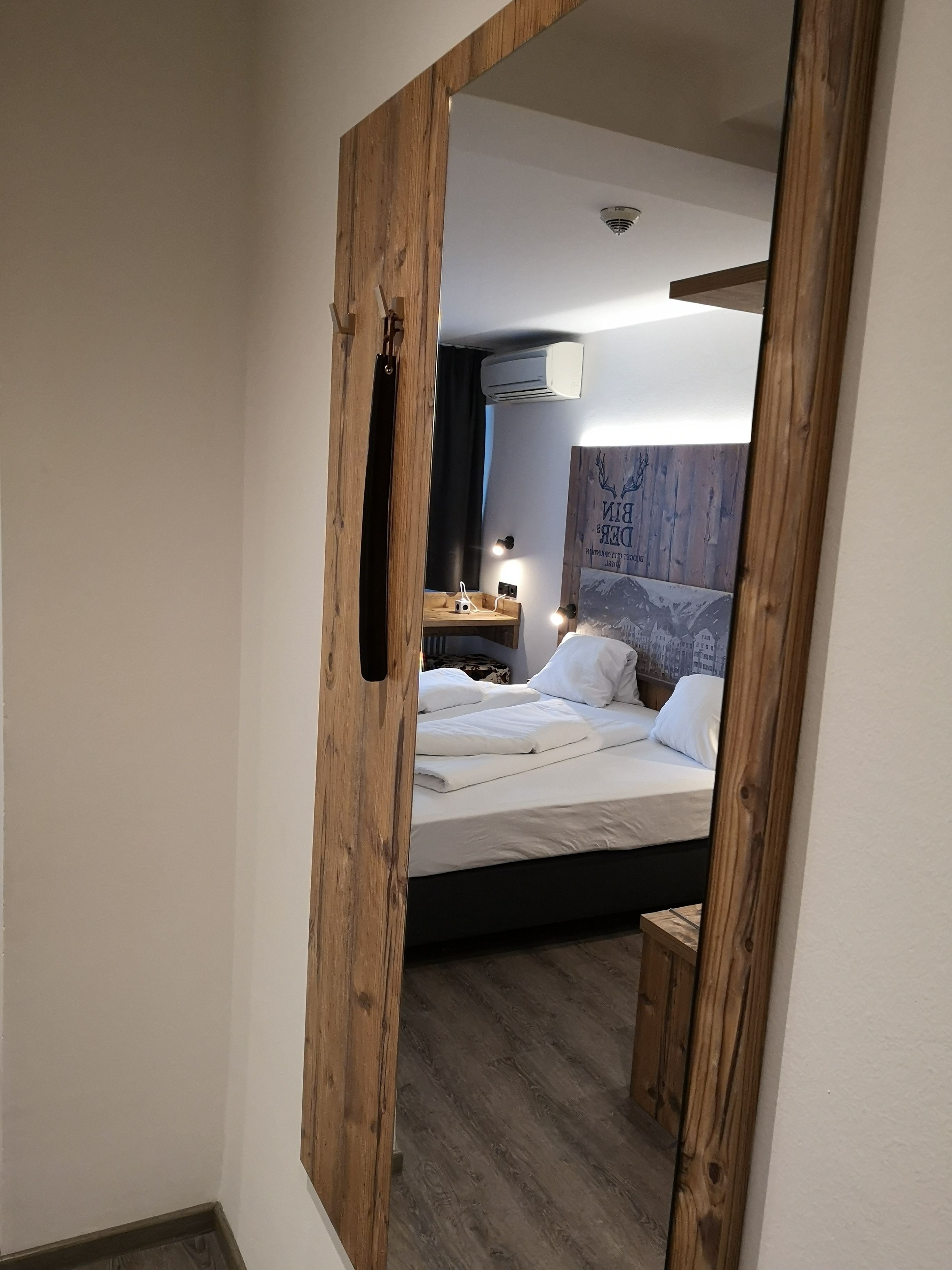 Ein Schlafzimmer mit einem hölzernen Kopfteil, einem Bett mit weißen Leinentüchern, einem Nachttisch mit Lampe und einem kleinen Holzschemel.