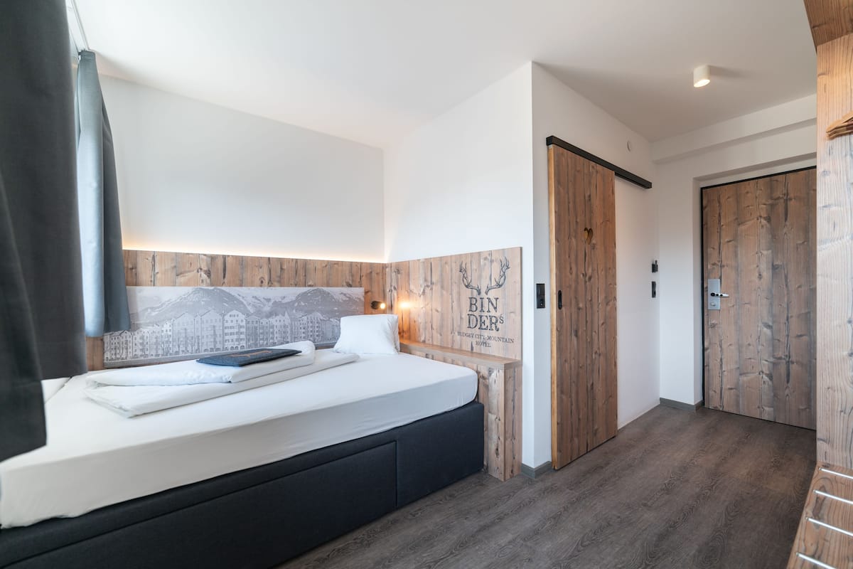 Habitación de hotel moderna con una cama grande, paneles de madera en las paredes y una obra de arte con un paisaje urbano sobre la cama.