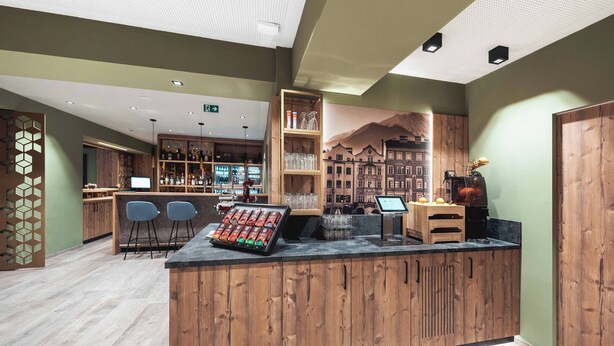 Een bar met houten toonbanken, barstoelen en gevulde flessenrekken.