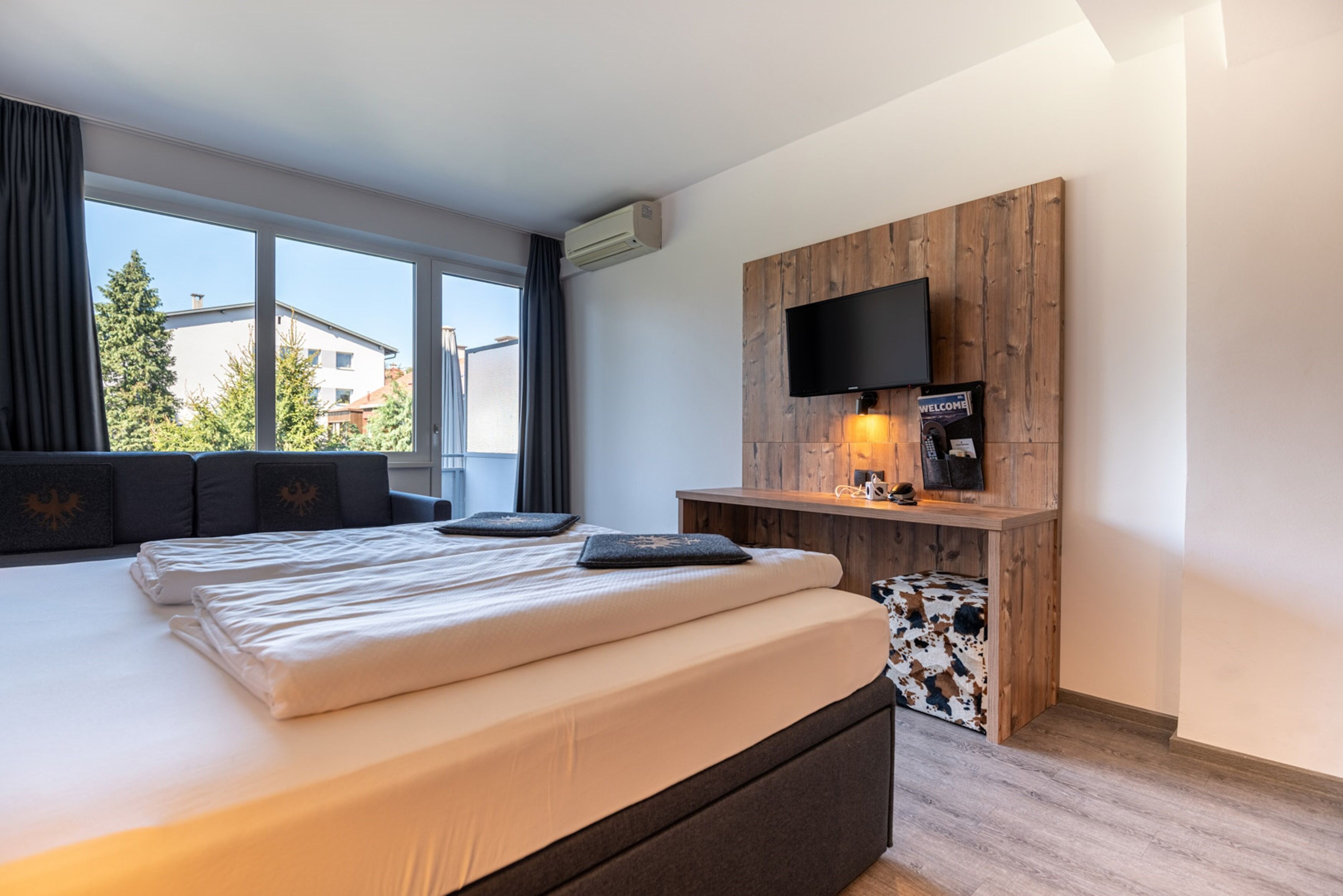 Moderni hotellihuone, jossa on suuri sänky, seinälle asennettu televisio ja puusta tehty koristeellinen seinä.