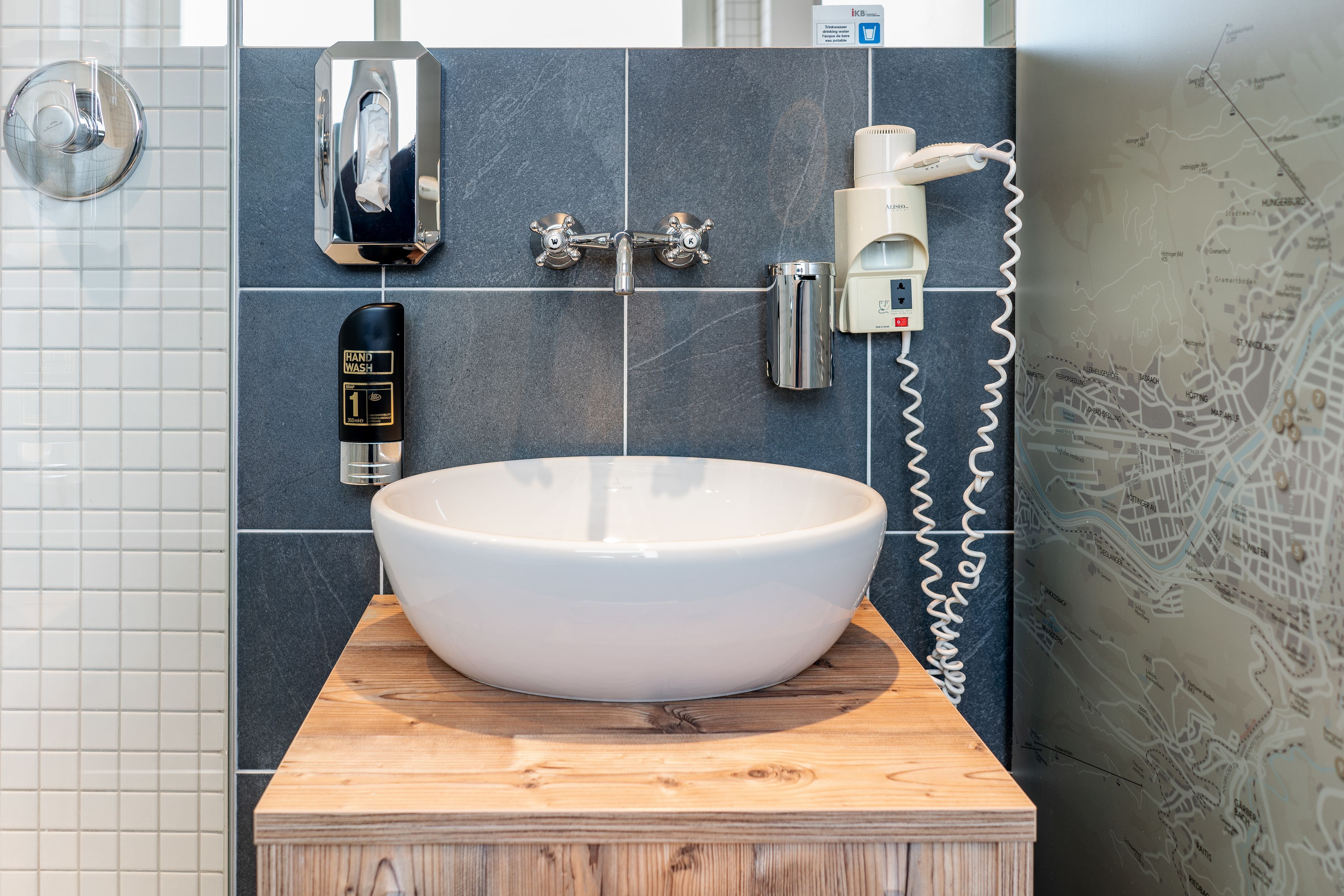 A bathroom with a large white sink on a wooden countertop, a hand dryer, a paper towel dispenser, and a hand soap dispenser.