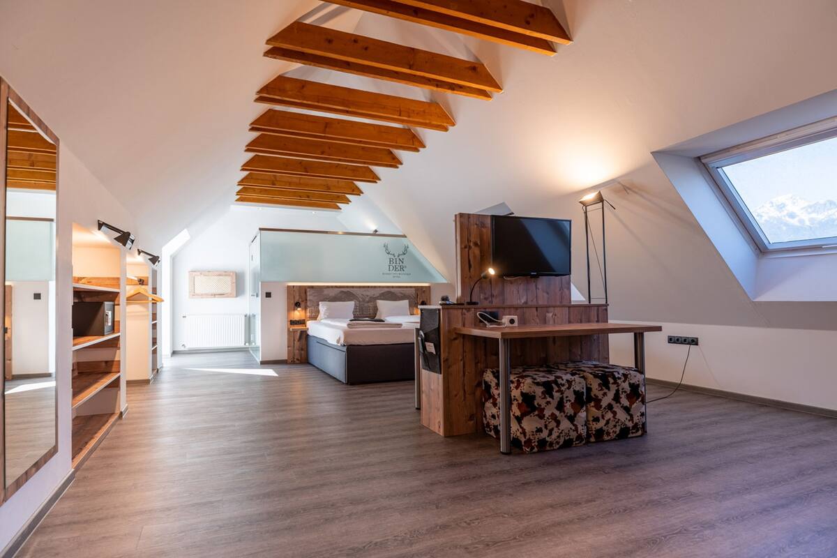 Un dormitorio tipo loft moderno con techo inclinado, una cama, un escritorio y un ventanal grande.
