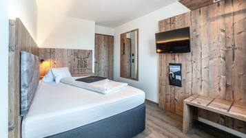 A modern bedroom with a large bed, wooden wall paneling, a mounted TV, and a bench.