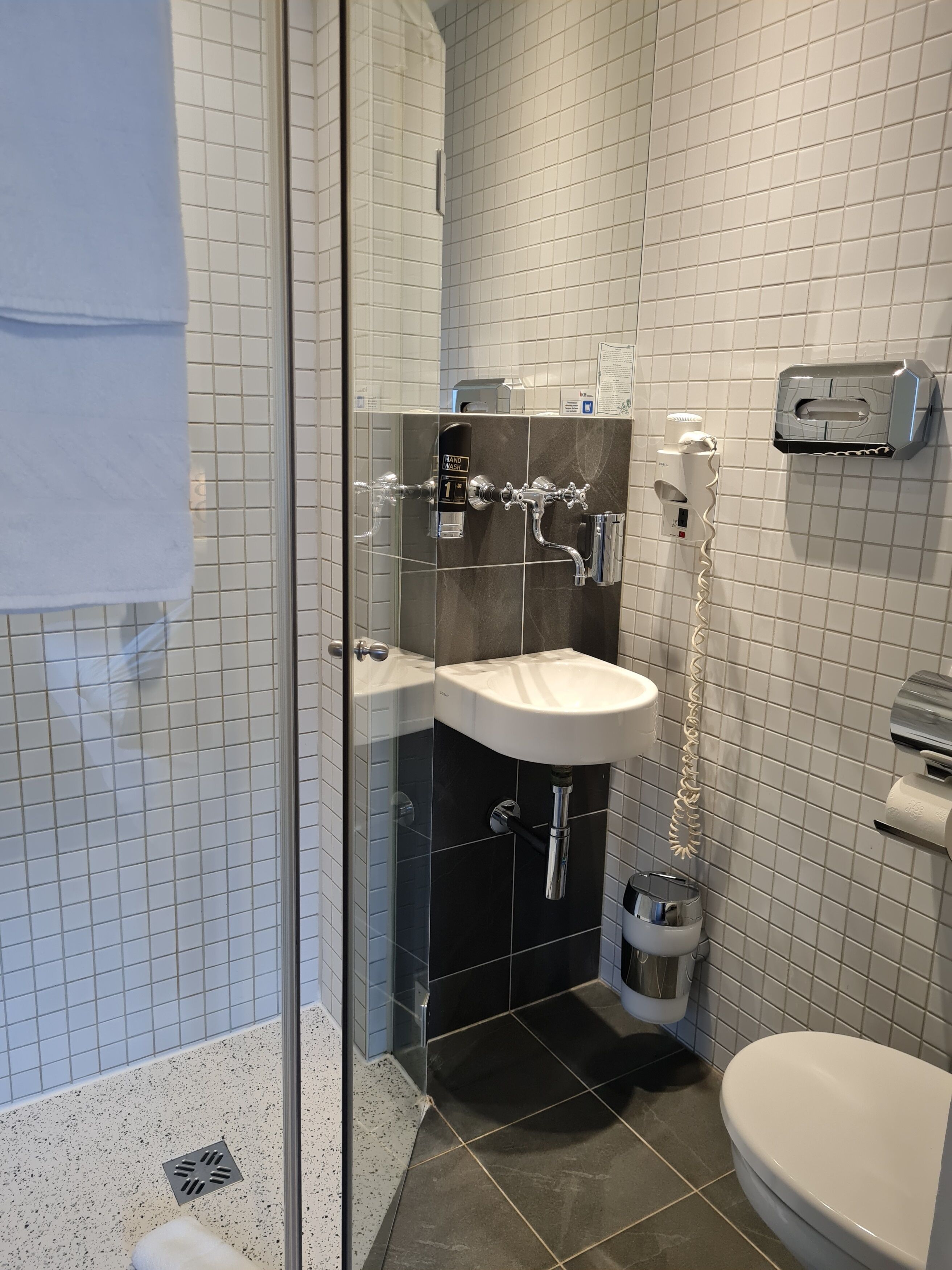Un baño moderno con cabina de ducha de vidrio, un lavabo blanco y un inodoro.