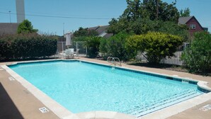 A rectangular swimming pool with clear blue water, surrounded by a concrete deck and a metal fence. - America's Inn - Houston (Houston)