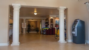 A hotel lobby with a reception desk, a self-service kiosk, and a luggage cart. - America's Inn - Houston (Houston)