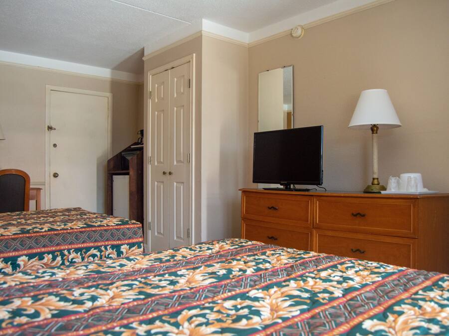 Una camera d'albergo con due letti, una televisione su un comò, una lampada e una porta.