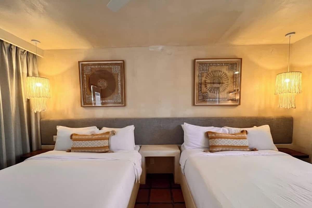 A hotel room with two beds, a nightstand, and two wall-mounted lamps.