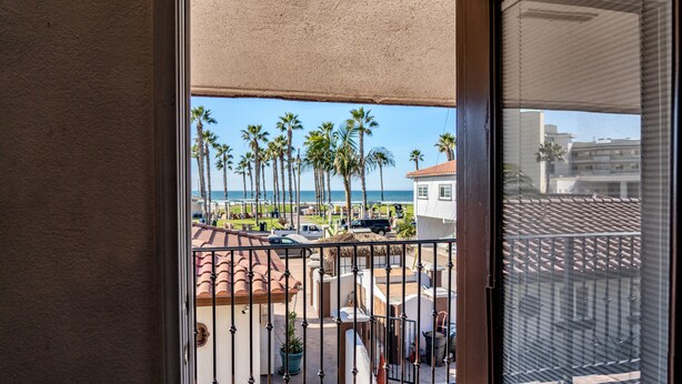 A balcony with a view of the beach, palm trees, and a parking area. - Los Bungalows (Imperial Beach)