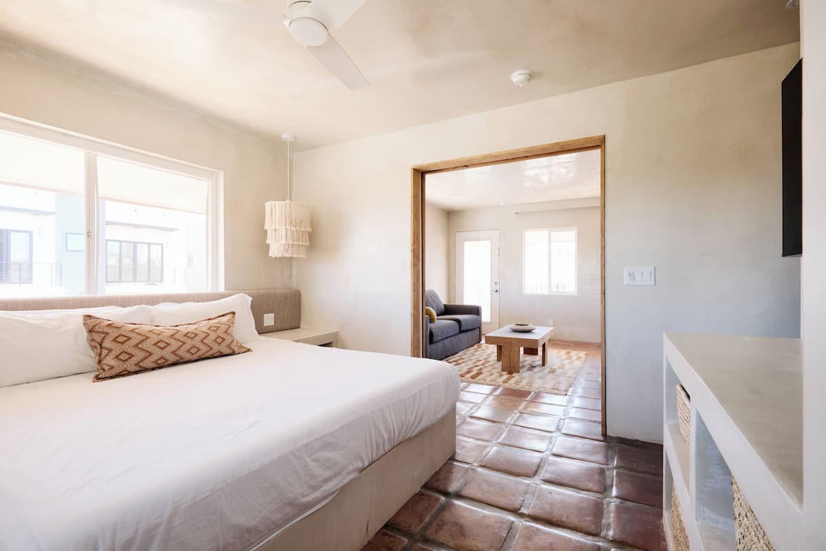 A bedroom with a bed, a ceiling fan, a window, and a door leading to another room.