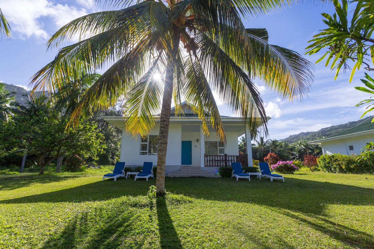 Une maison à l’extérieur blanc, avec une porte bleue et une véranda dotée de chaises bleues.
