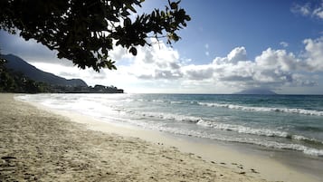 A beach with clear skies, gentle waves, and a mountain in the background.