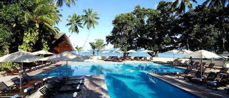 A pool area with lounge chairs and umbrellas, surrounded by palm trees.
