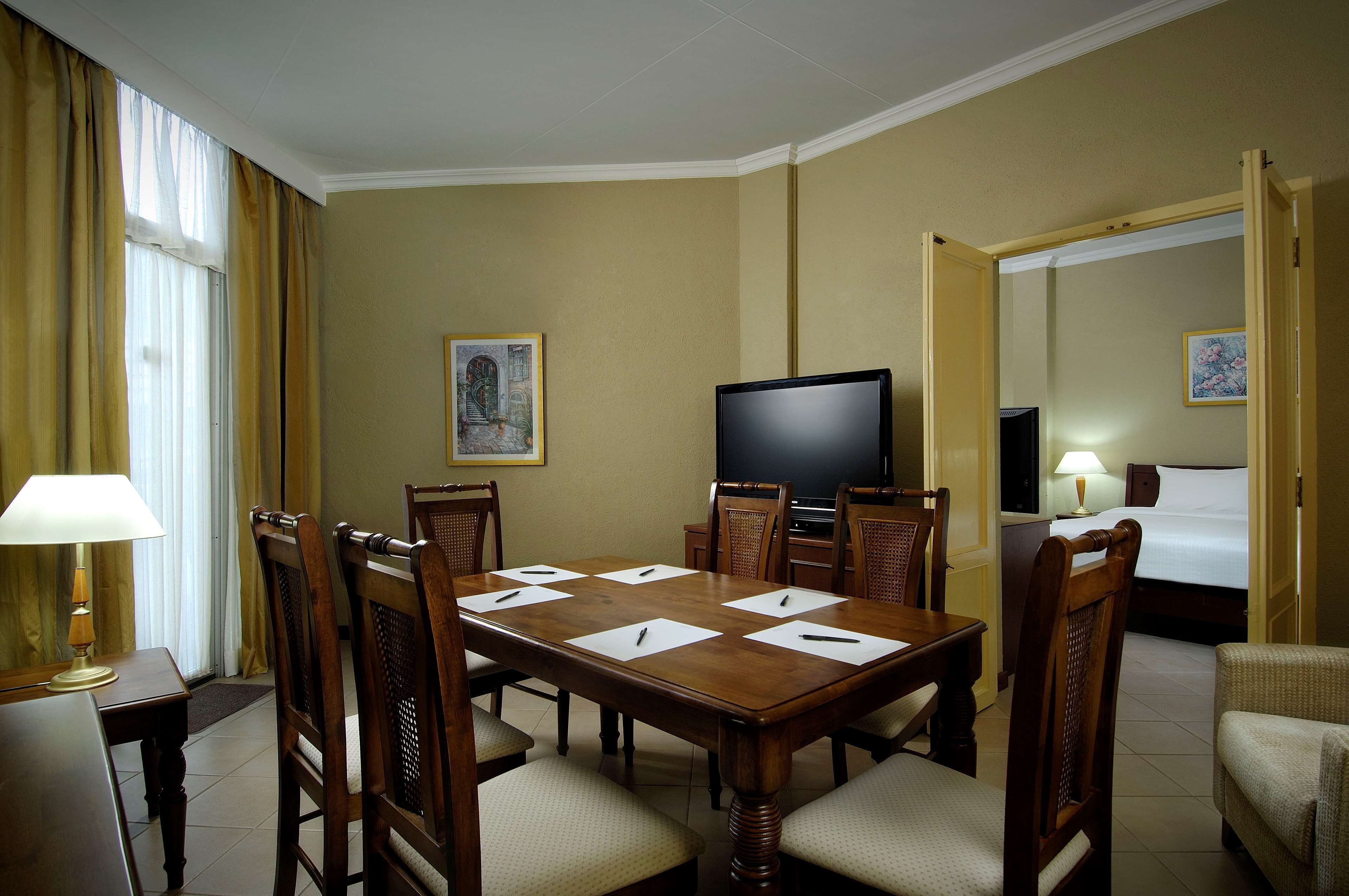Een hotelkamer met een grote houten eettafel, vier stoelen, een televisie, een bed en een kleine bank.