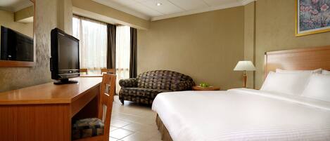 A hotel room with a bed, a desk with a television, a chair, a lamp, and a painting on the wall.