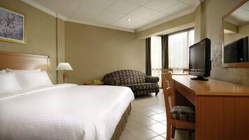Habitación de hotel con una cama grande, un escritorio con televisor, una silla y una ventana con cortinas.