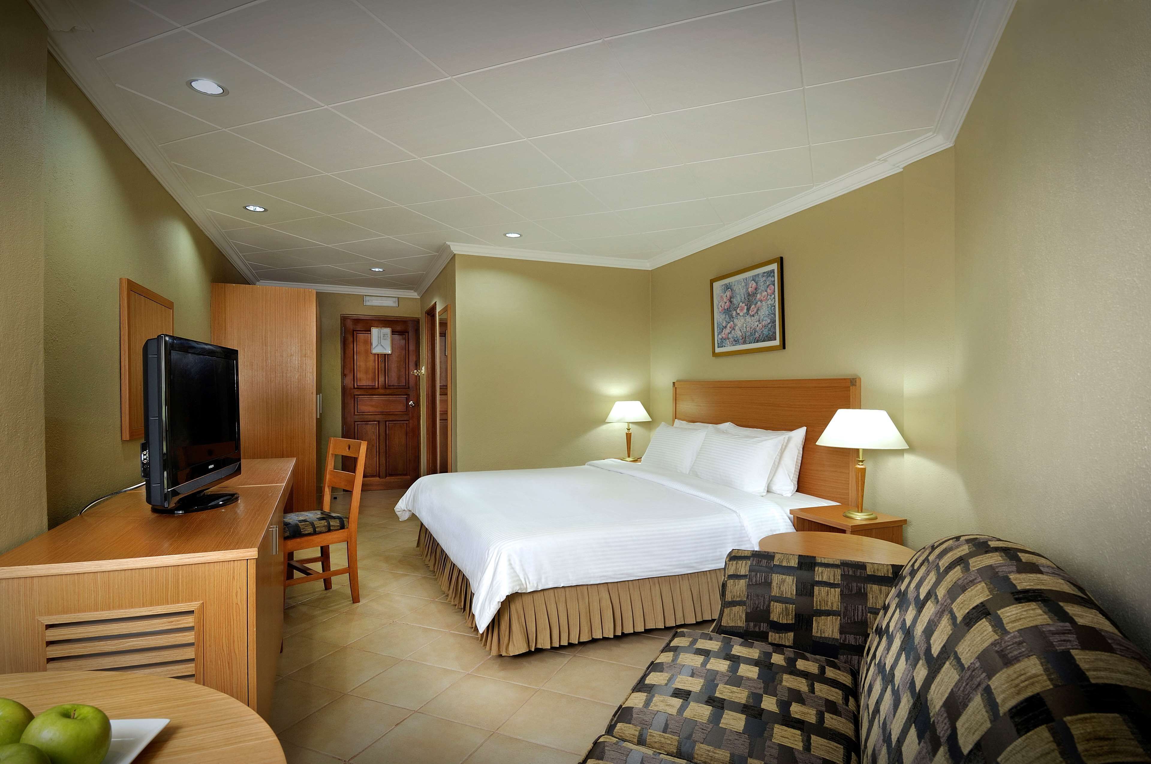 A hotel room with a bed, a TV on a desk, a chair, a sofa, and a lamp.