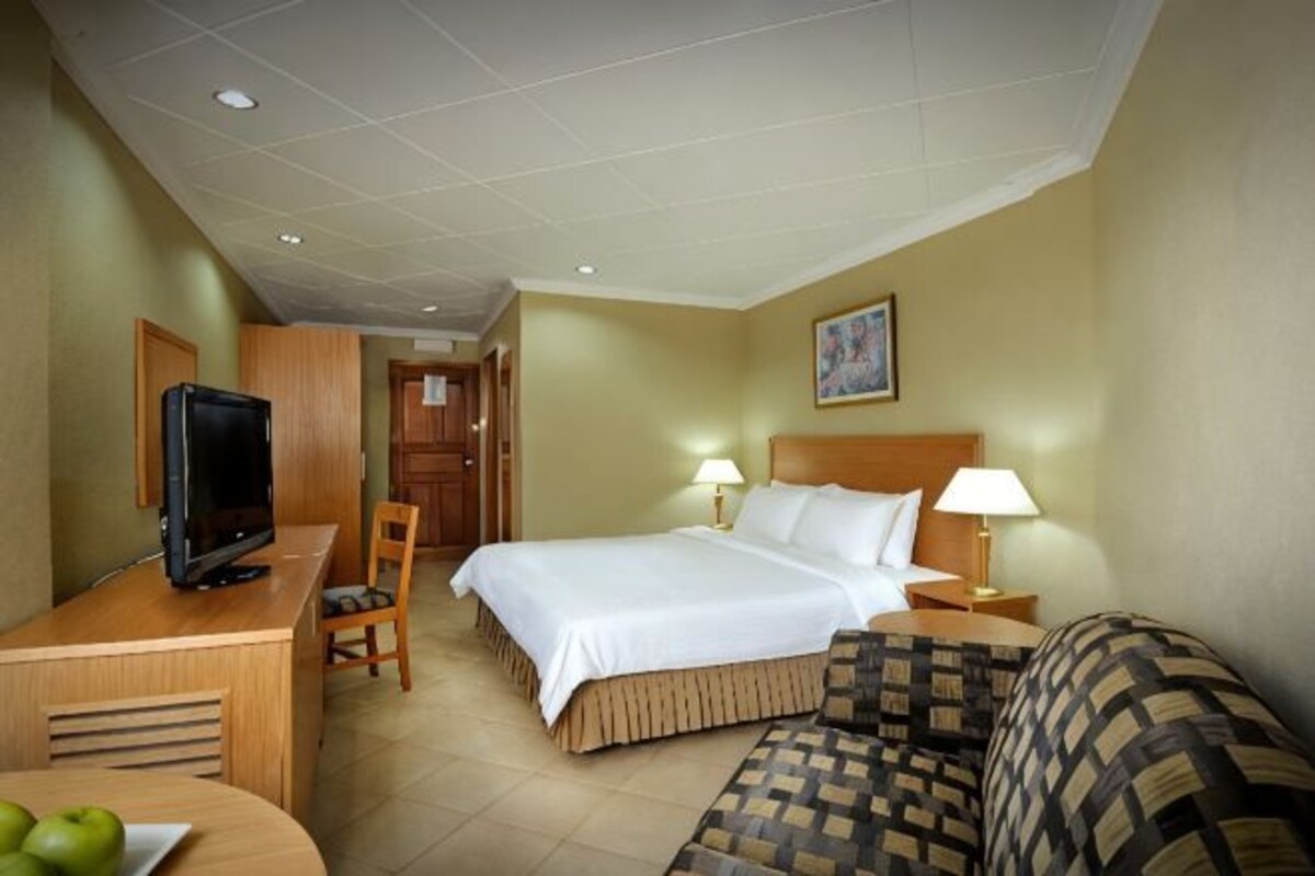 A hotel room with a bed, a desk with a television, a chair, a lamp, and a couch.