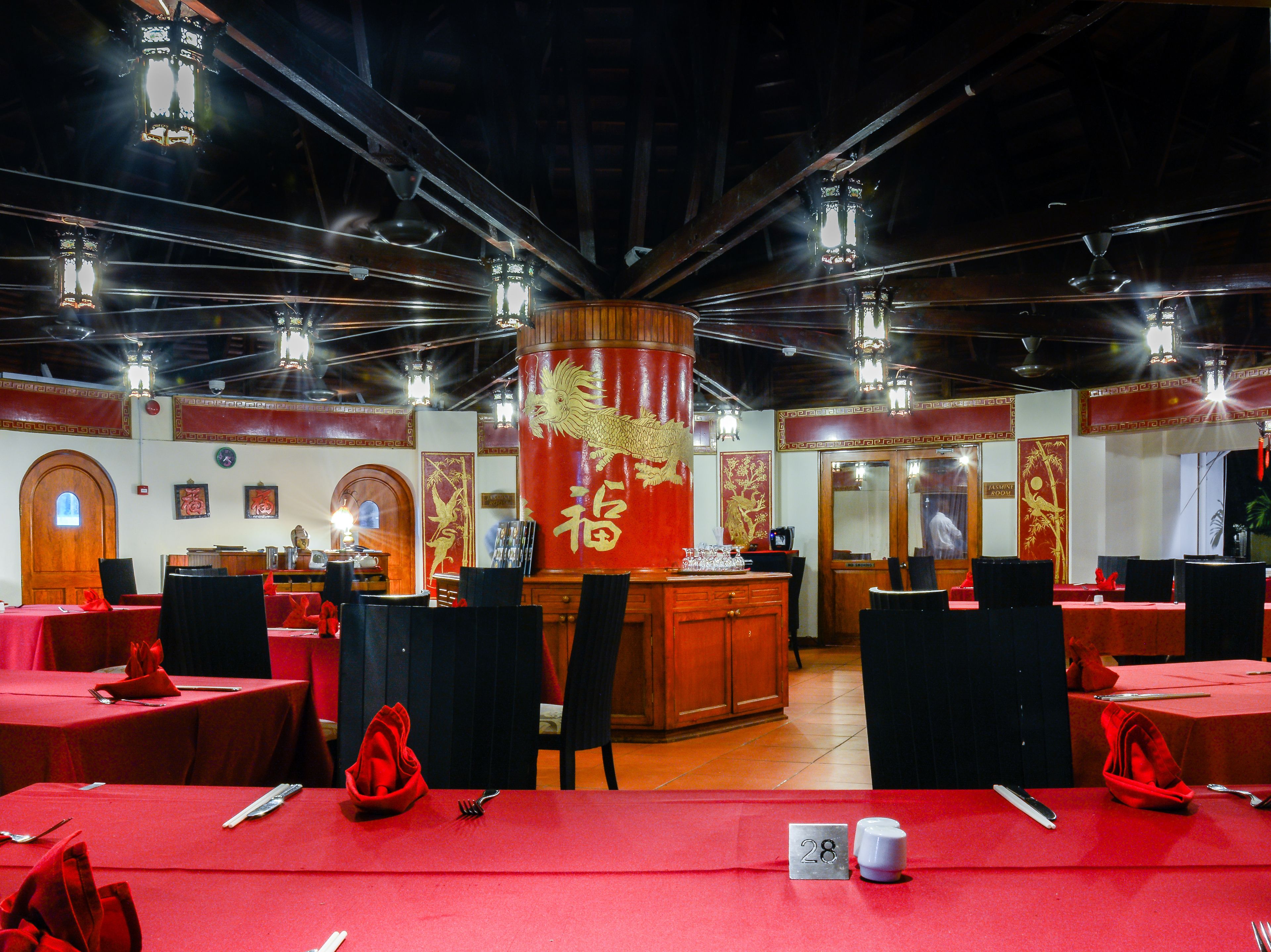 A restaurant with red tablecloths, wooden chairs, and a central decorative pillar.