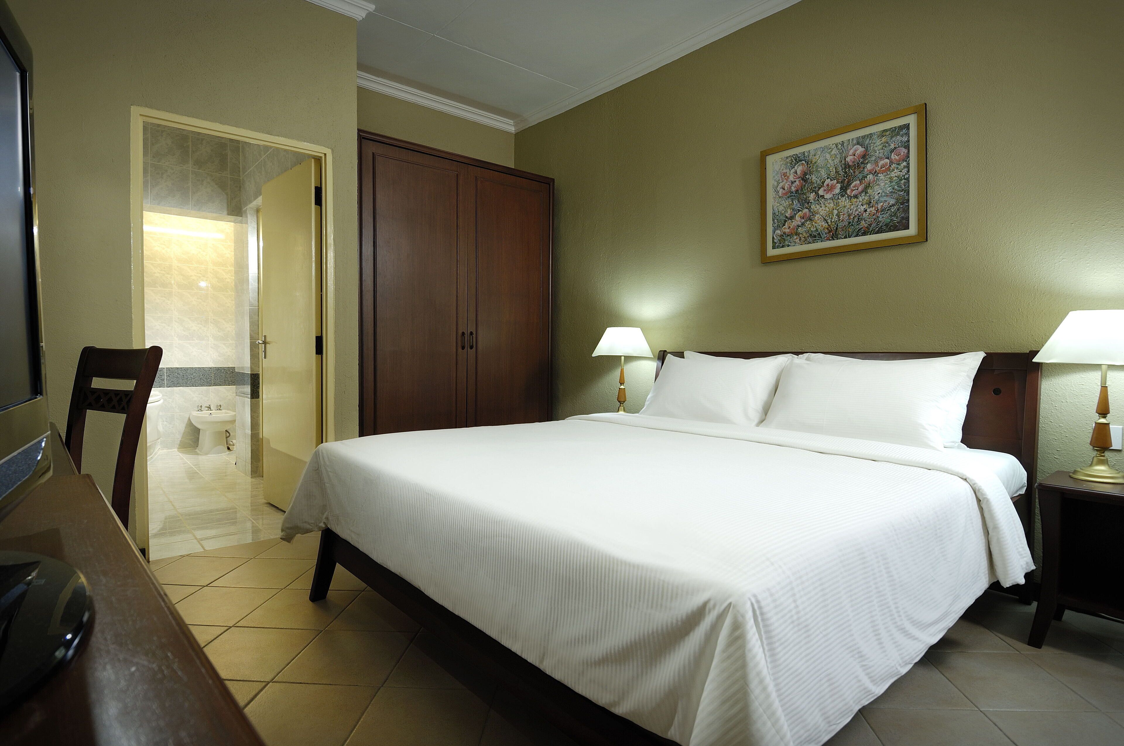 Une chambre d’hôtel avec un grand lit, deux lampes de chevet, une armoire en bois et une salle de bain visible à travers une porte ouverte.