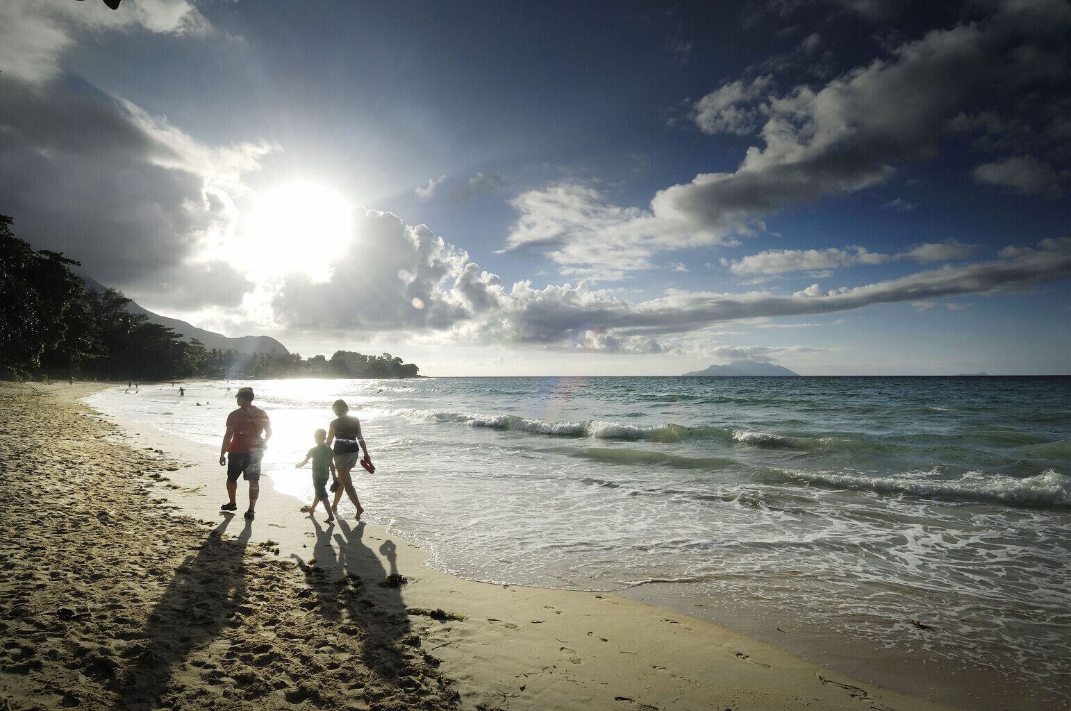 A beach scene with a clear sky, sun, and ocean waves.