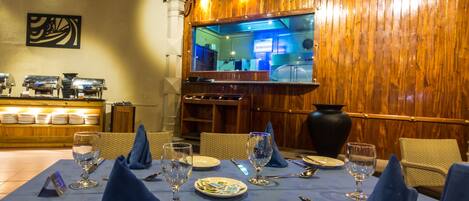 A restaurant with a wooden interior, a bar area, and a dining table set with blue napkins, plates, and cutlery.