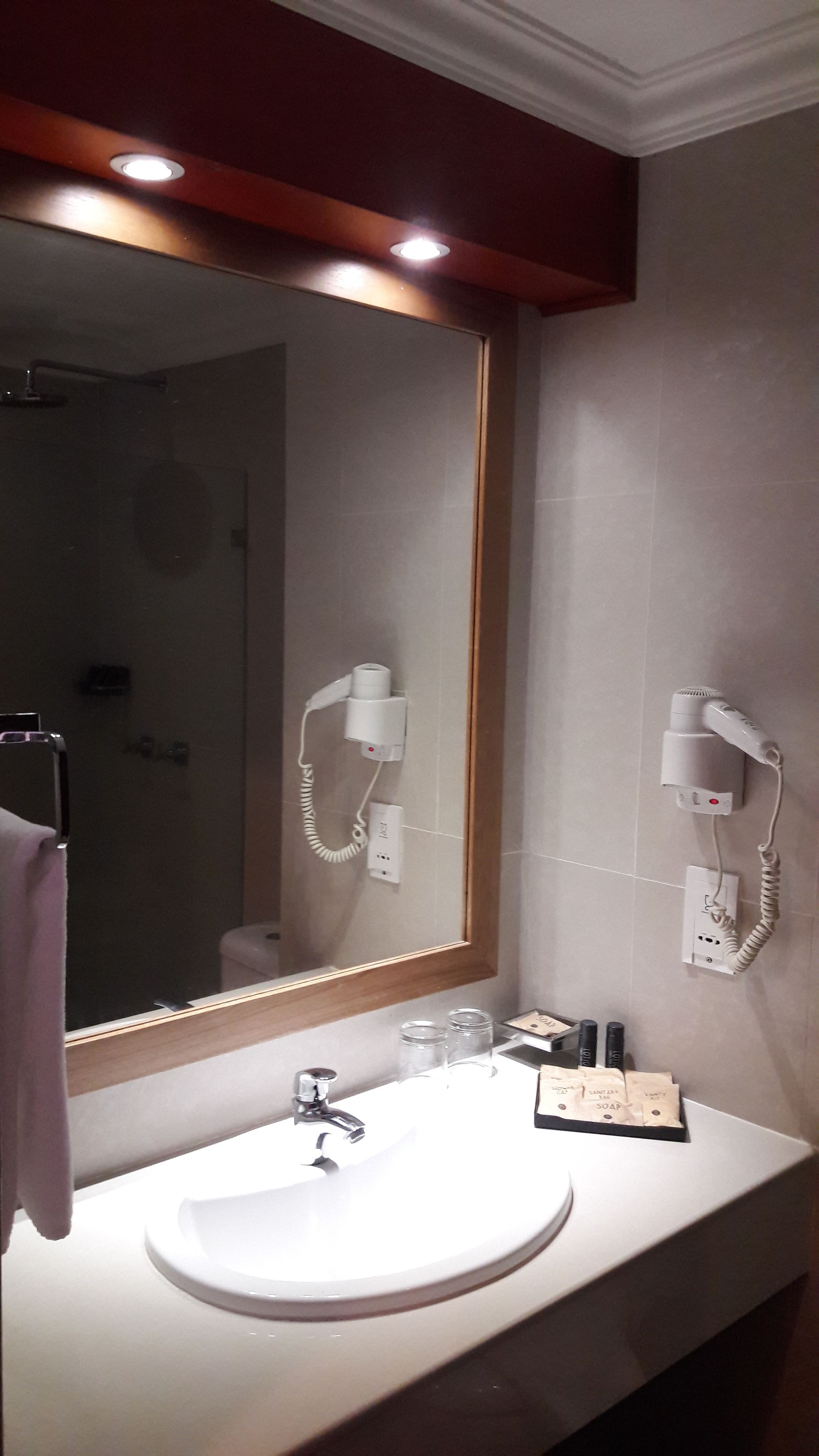 A bathroom with a large mirror, a sink, and two hair dryers mounted on the wall.
