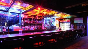 A bar with a neon-lit ceiling, shelves of bottles, and a Coca-Cola refrigerator.
