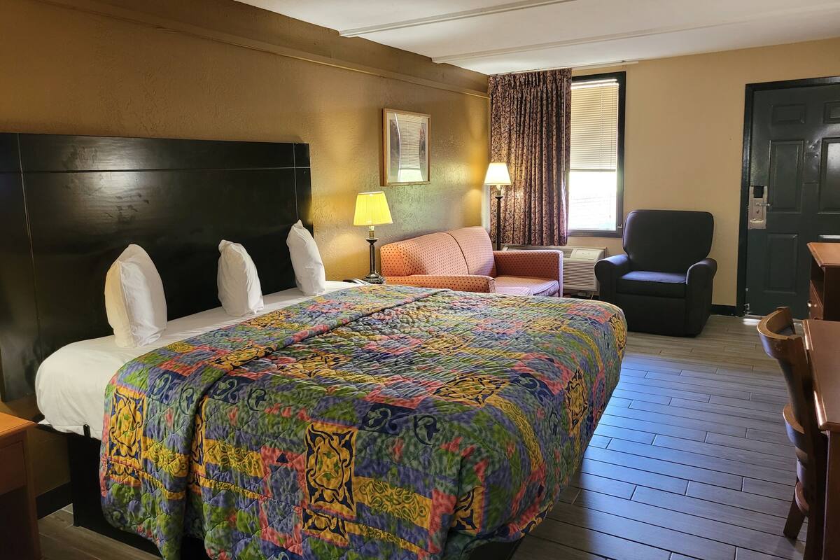 Une chambre d’hôtel avec un grand lit, un bureau, deux chaises, une lampe et une fenêtre avec des rideaux.