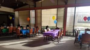 A covered outdoor dining area with tables and chairs, large windows, and balloons.