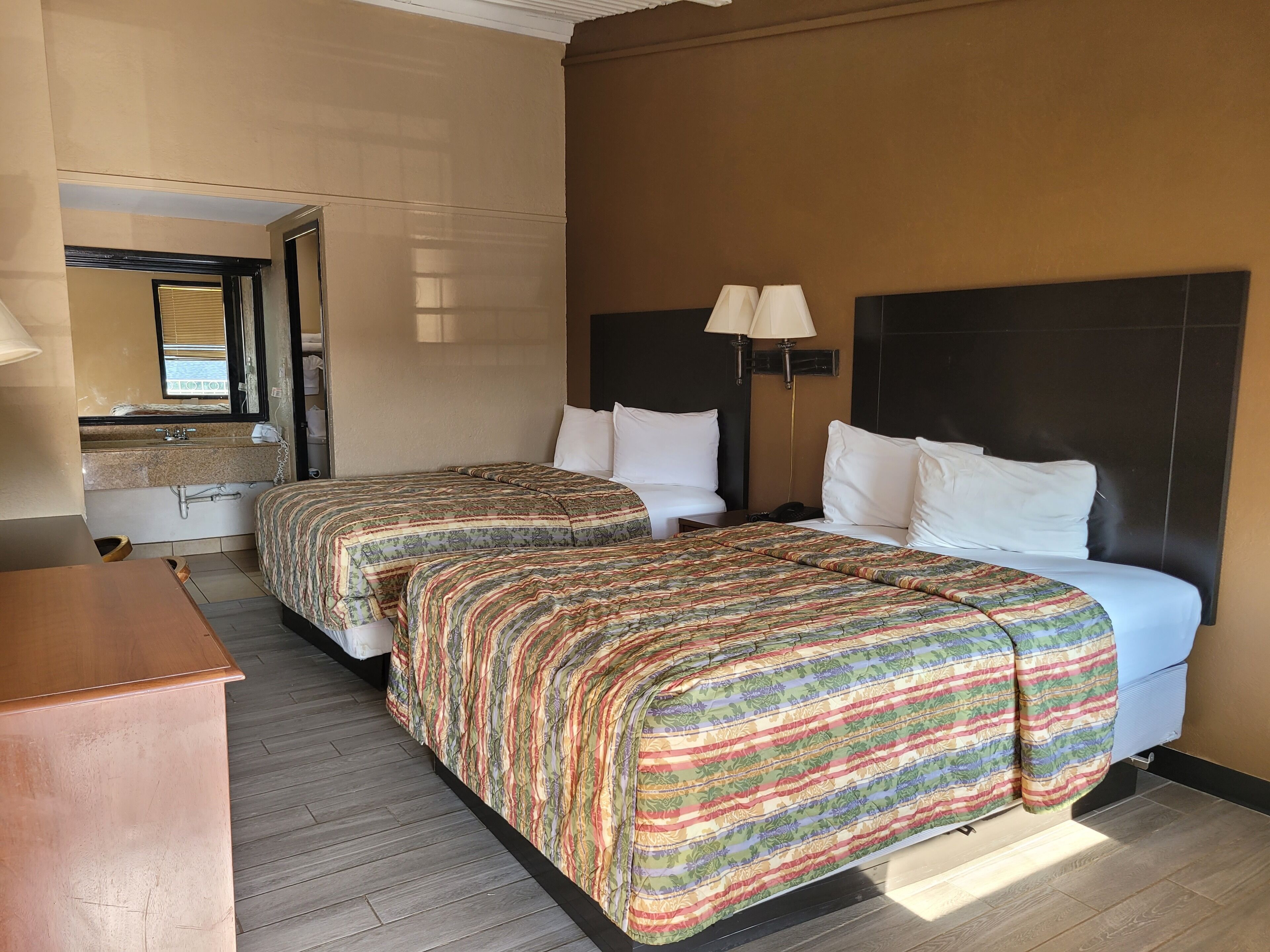 A hotel room with two beds, a bathroom, and a desk.