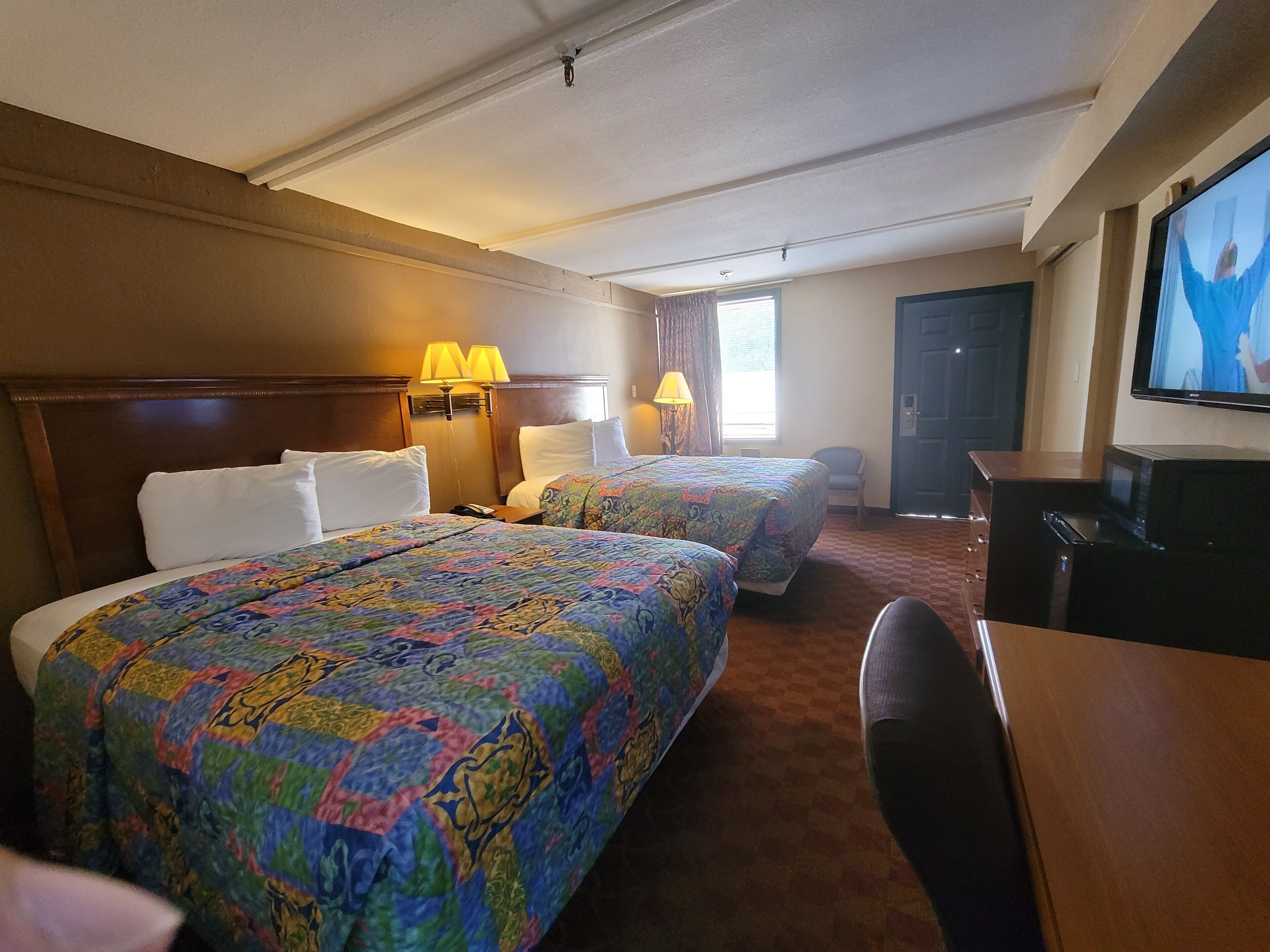 A hotel room with two beds, a desk, a television, and a door.