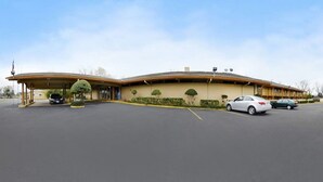 A motel with a curved roof, a covered parking area, and a row of trees along the facade.