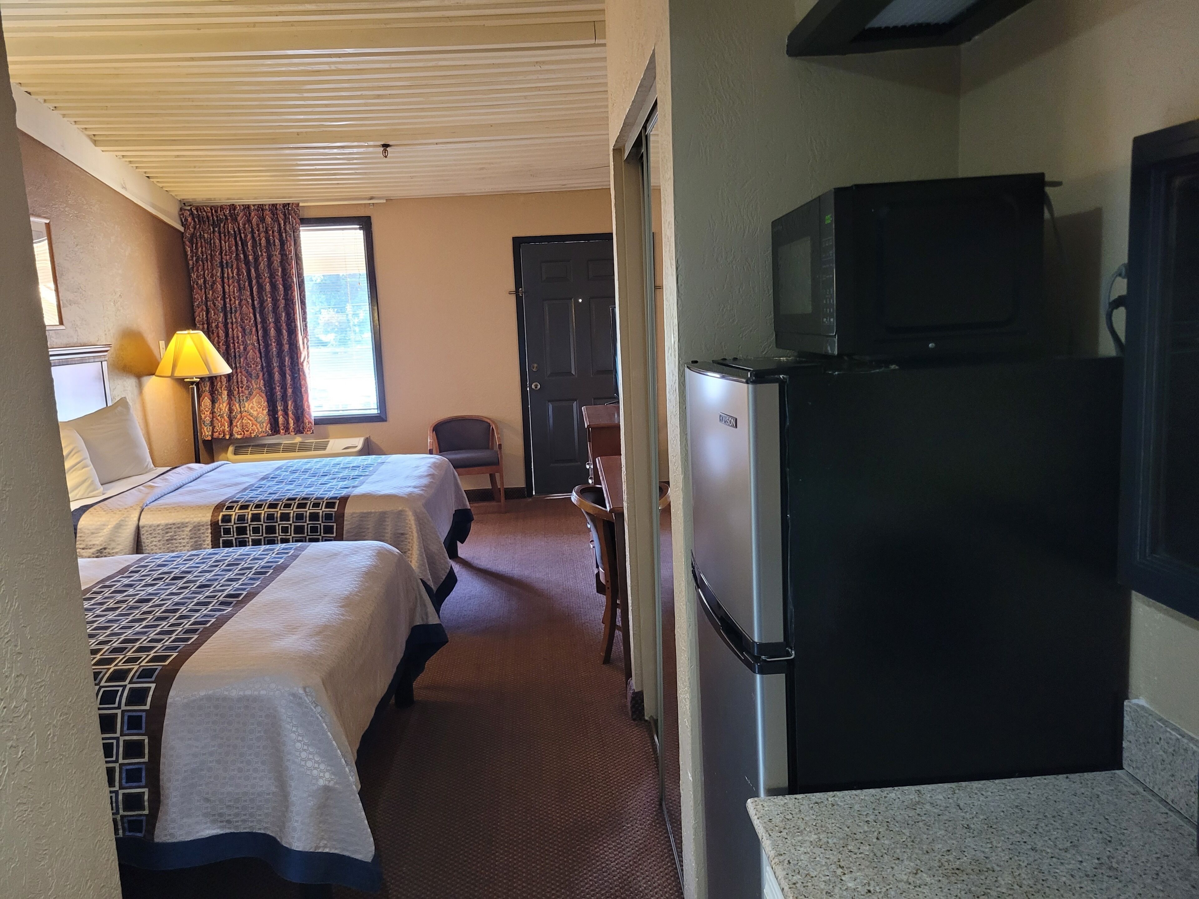 A hotel room with two beds, a refrigerator, a microwave, and a television.