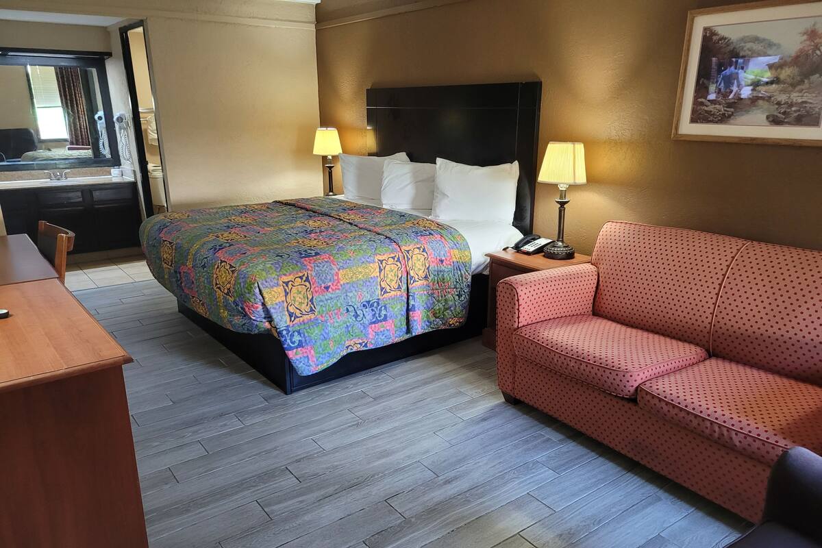 Une chambre d’hôtel avec un lit, un canapé rouge, un bureau et deux lampes de chevet.