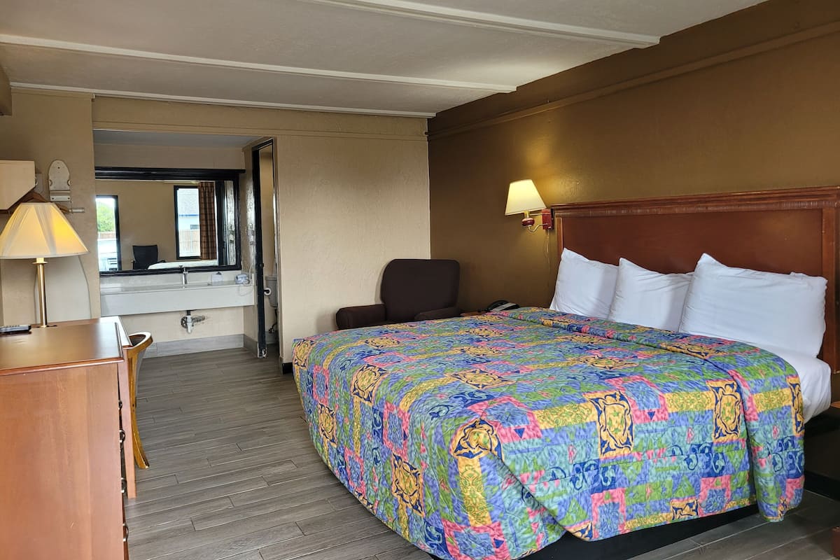 Une chambre d’hôtel avec un lit, une chaise, un bureau, une lampe et un miroir.