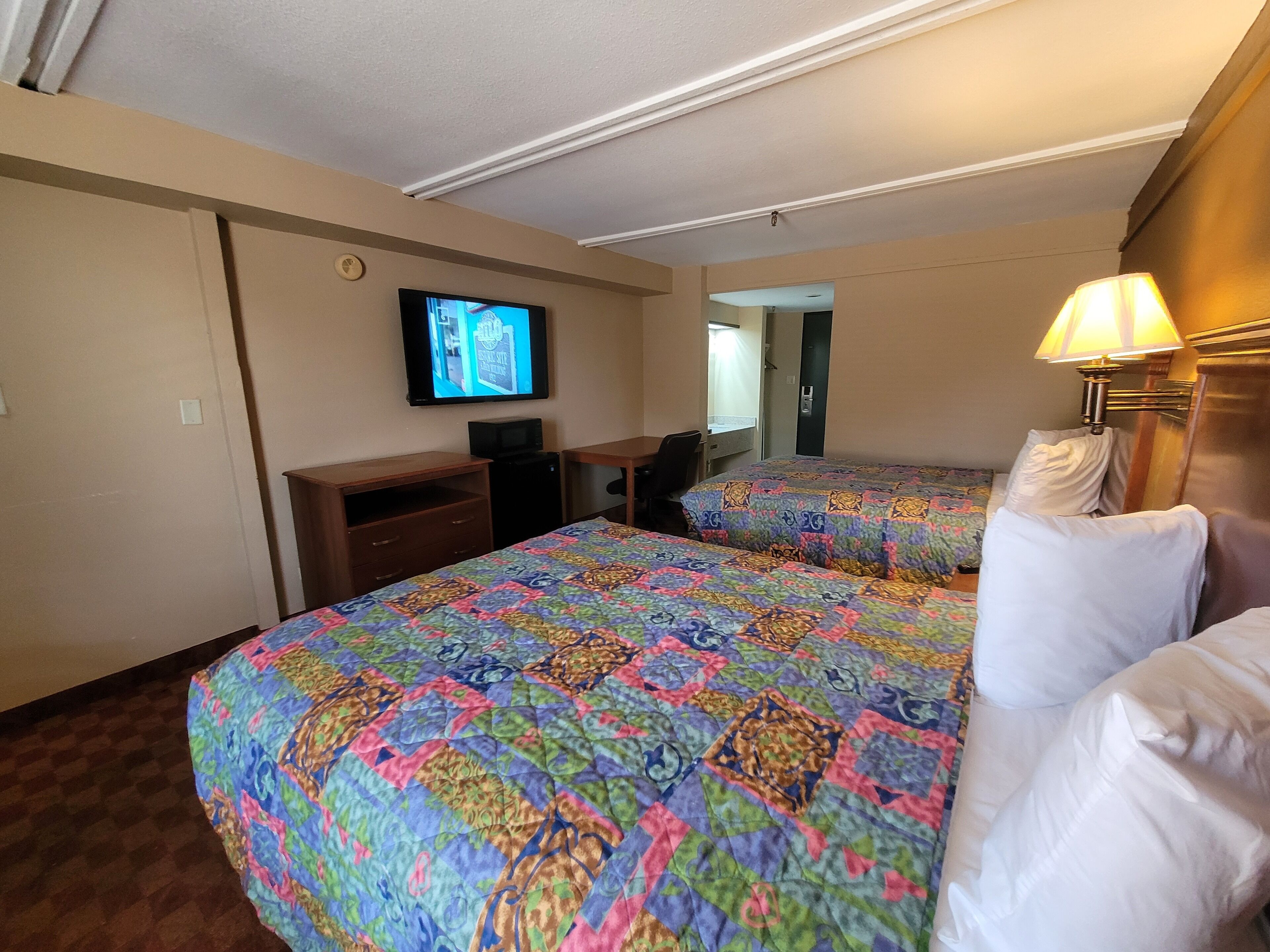 Una habitación de hotel con dos camas, un escritorio, un televisor y una lámpara.