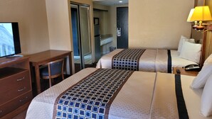 A hotel room with two beds, a desk, a TV, and a bathroom visible through an open door.