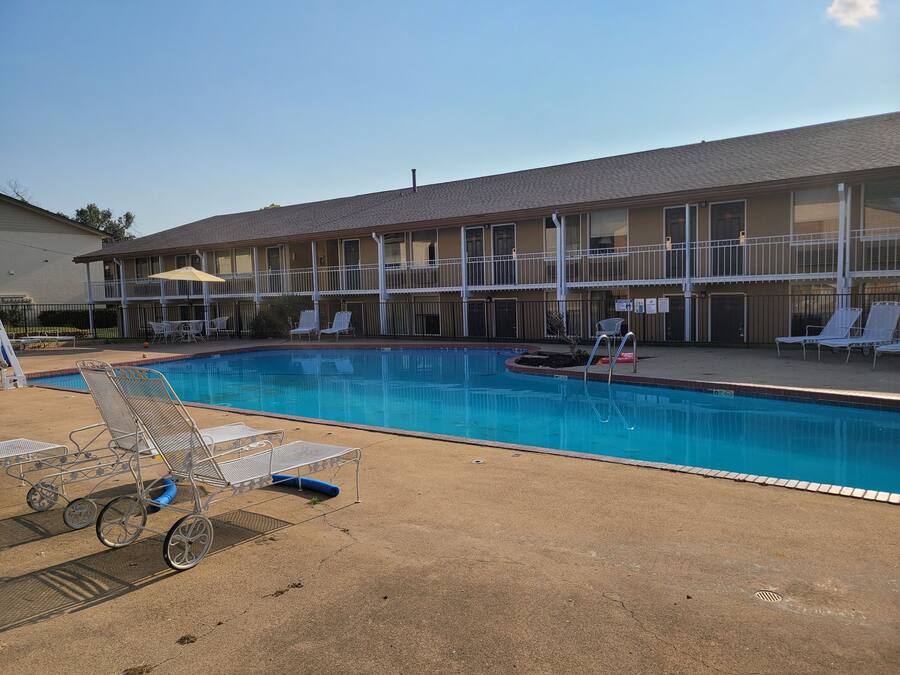 A hotel with a swimming pool, lounge chairs, and a covered patio area.