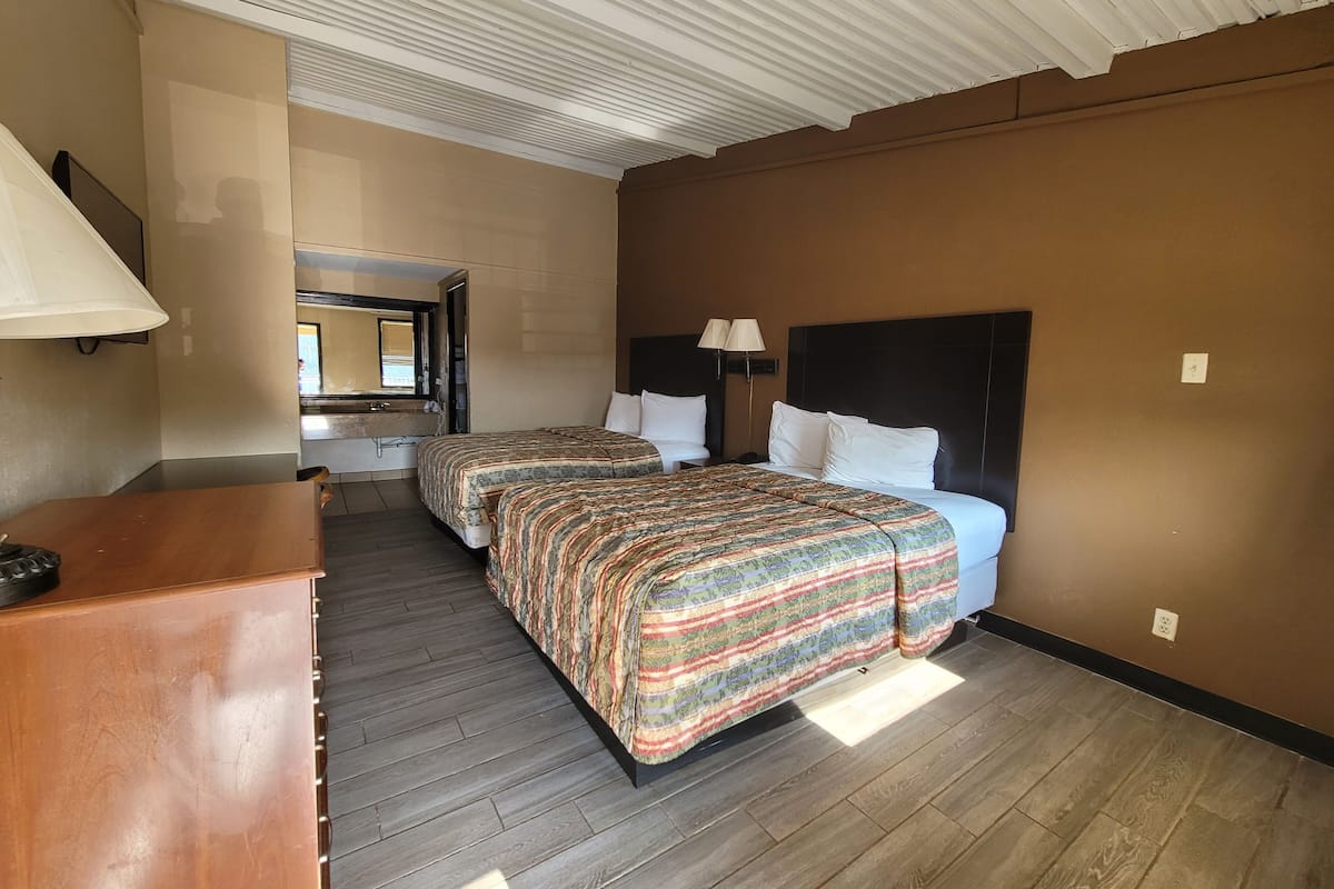 Une chambre d’hôtel avec deux lits, une commode en bois, une salle de bain avec un miroir et un plafond à motifs en relief.