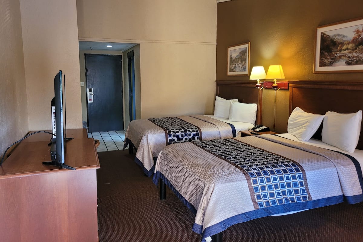 Une chambre d’hôtel avec deux lits, un bureau avec une télévision et une lampe.