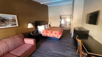 A hotel room with a bed, a desk, a chair, a sofa, a lamp, a telephone, and a painting on the wall.
